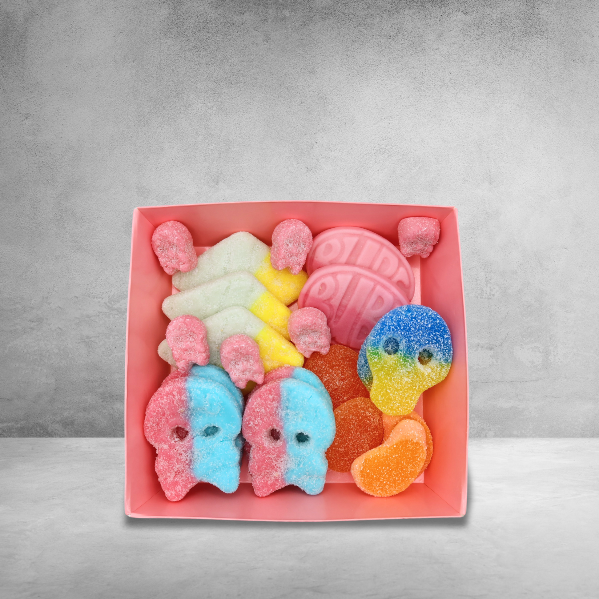 A pink gift box filled with various colorful Swedish gummy candies, including sweet and sour skulls.