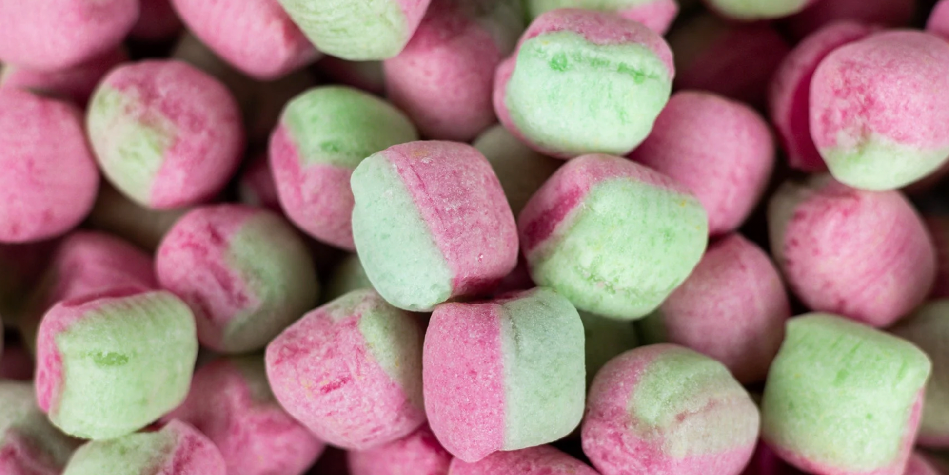 A close-up image of sour melon flavored hard candies, primarily pink and green in color, with a textured surface.