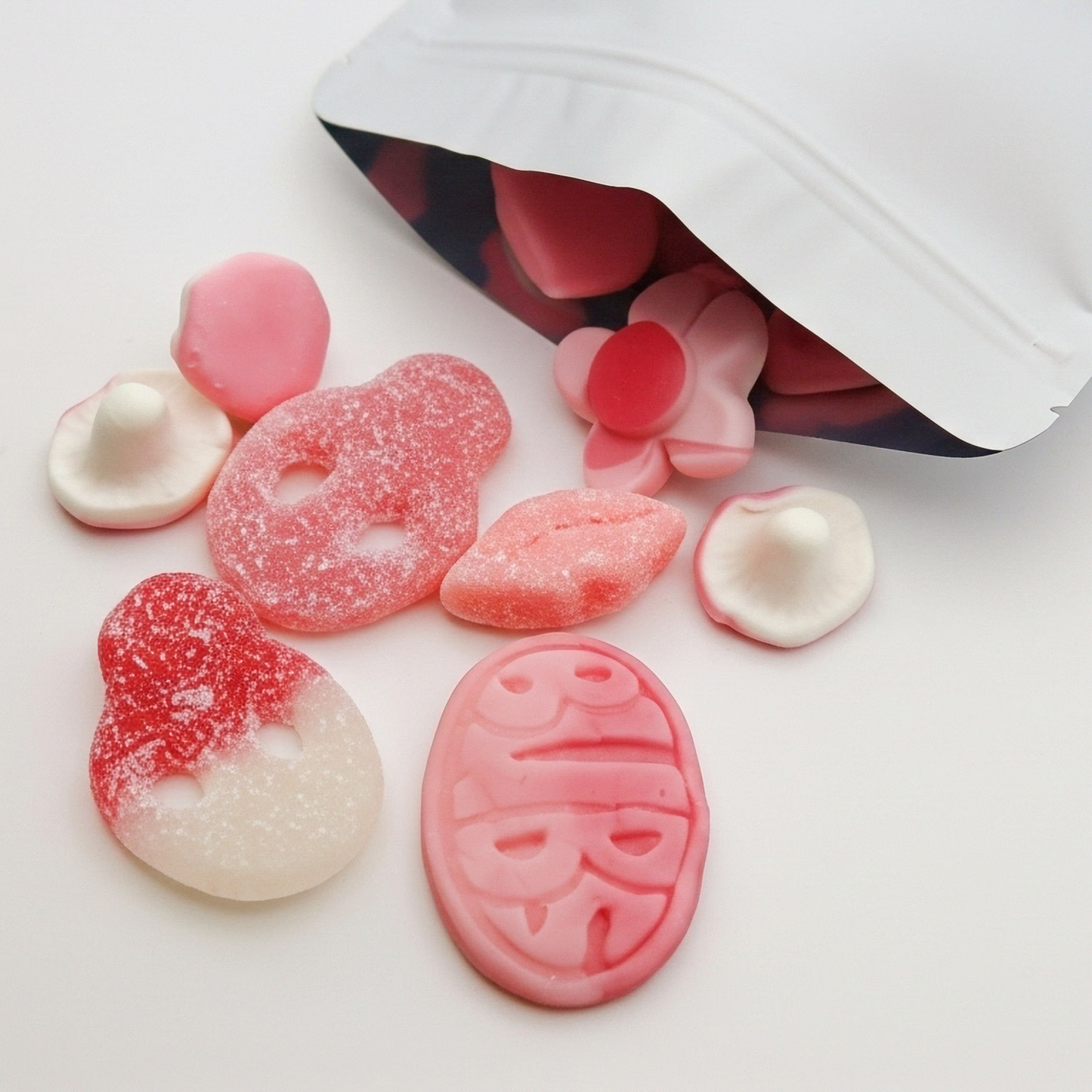 Colorful gummy candies spilling out of a white bag on a light background